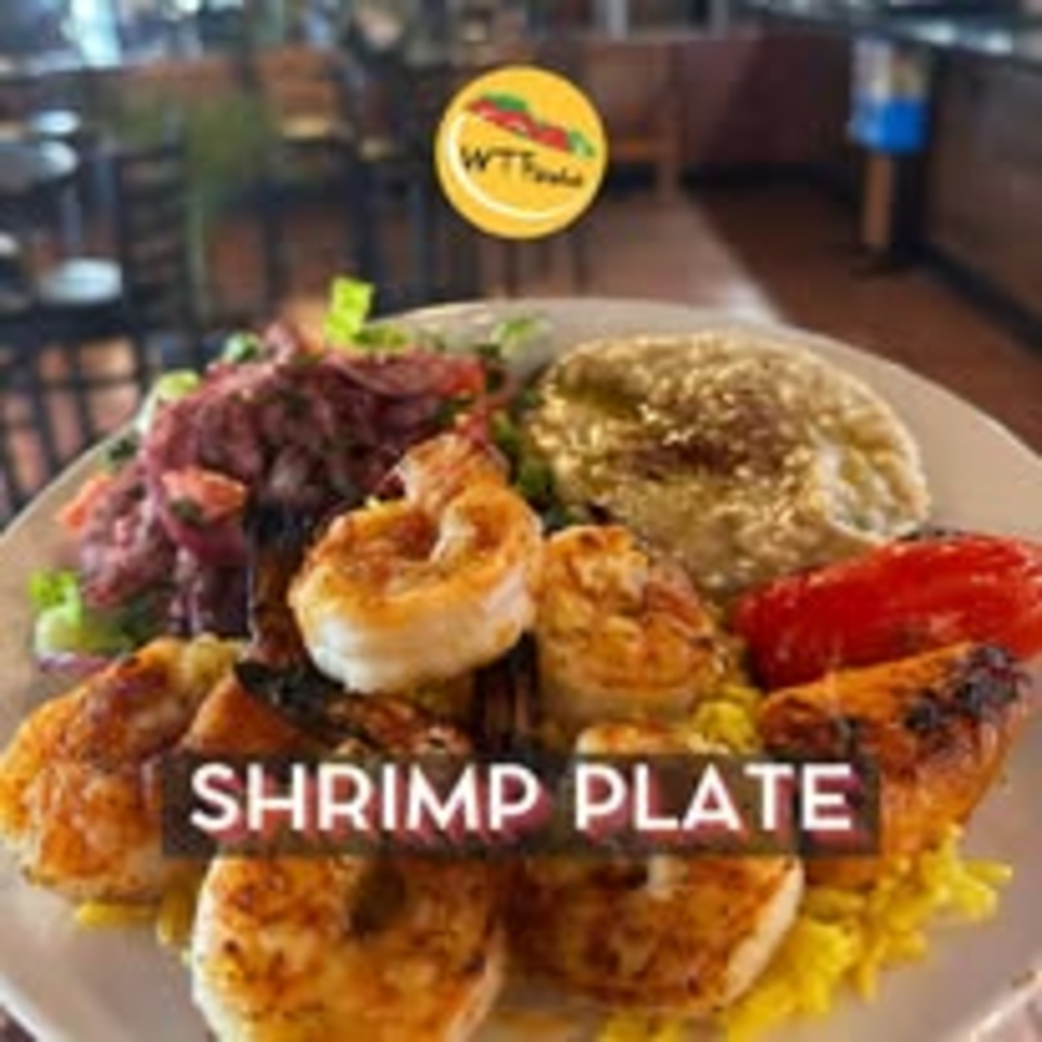 A platter of grilled shrimp with rice, salad, vegetables, and sauces in a restaurant setting.